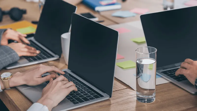 Pessoas trabalhando em seus laptops, com um ambiente de escritório compartilhado ao fundo