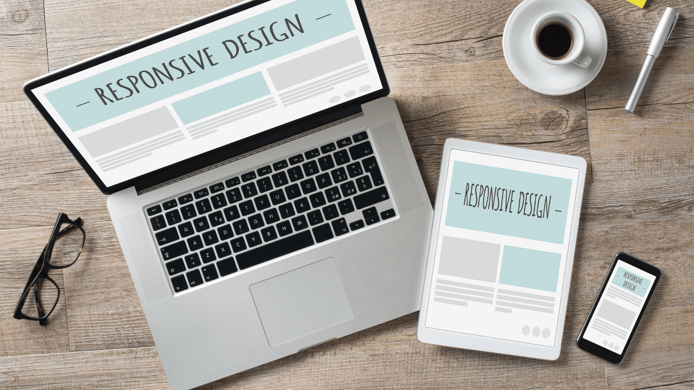 Imagem de um laptop, tablet e smartphone exibindo a mesma página com o texto 'Responsive Design'. A cena destaca a adaptação de desenvolver um site com design responsivo em diferentes dispositivos, incluindo um bloco de notas, óculos e uma xícara de café ao lado.
